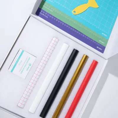 Open box of the iCraft™ Starter Pack showing a box of weeding tools, a roll of gid transfer tape, matt white heat transfer vinyl, glossy gold, matt black and red permanent adhesive vinyl. 3 cutting mats are placed in the lid.
