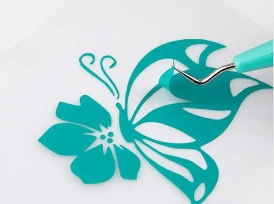 Close-up of a weeding hook pulling a piece of superfluous vinyl from a butterfly on a flower in tiffany blue permanent adhesive vinyl.