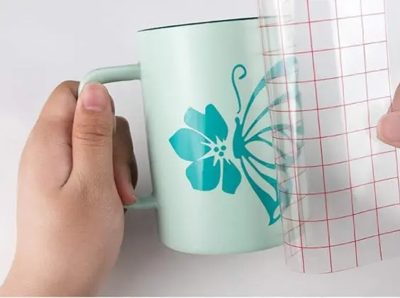 Grid transfer tape transferring a design in tiffany blue permanent adhesive vinyl on a mug.