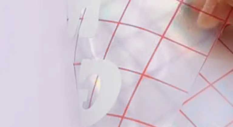 Close-up of a piece of grid transfer tape pulling a design from the PET backing.